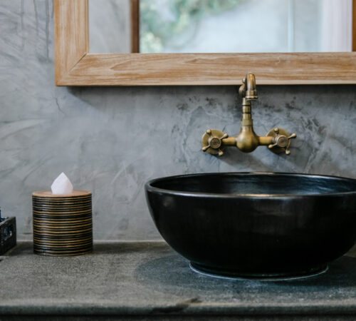 Black sink, vintage copper faucet, gray wall, mirror, loft bathroom interior details. Close up, minimalism concept